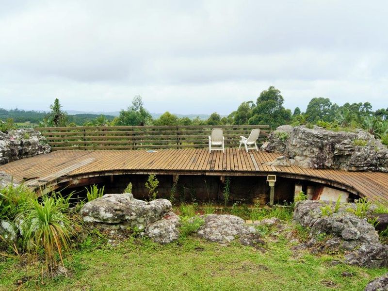 An elevated timber deck patio integrated with natural rock formations, offering expansive rural views and requiring maintenance to the decking and surrounding landscape.