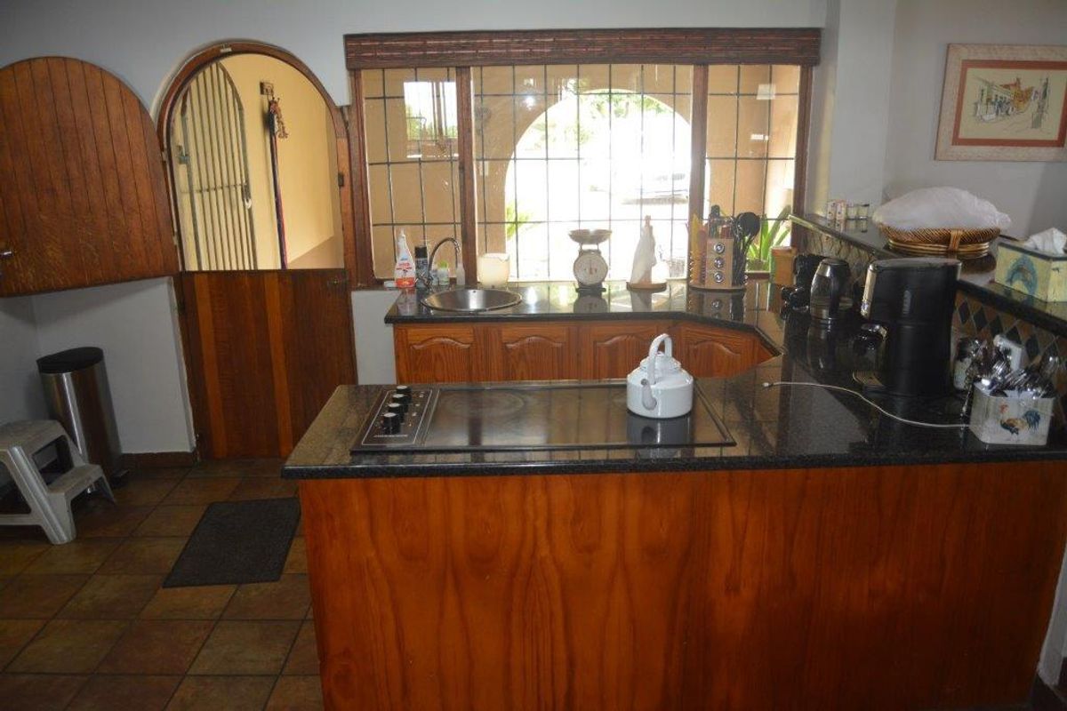 A rustic kitchen featuring wooden cabinetry, granite countertops, an integrated electric cooktop, and a distinctive stable-style door with leaded glass windows.