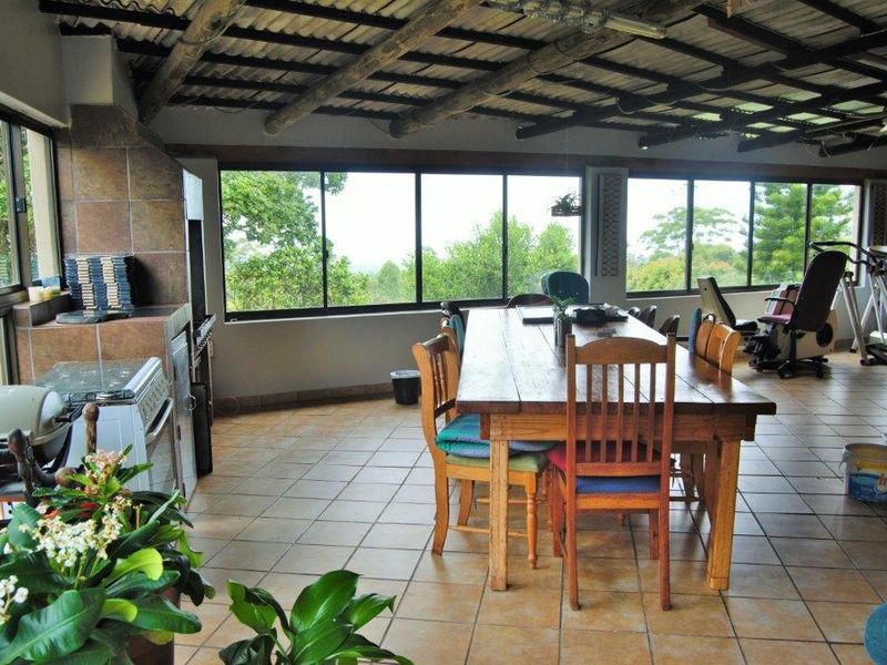 Spacious covered patio featuring a built-in braai, tiled flooring, and exposed timber beams, offering expansive views through large windows.