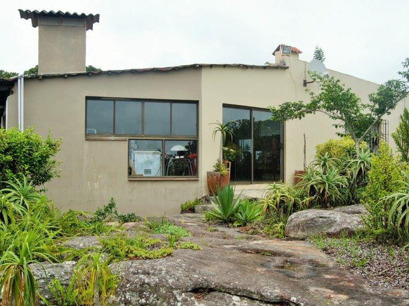 Rear elevation of a farm-style dwelling featuring a prominent chimney, sliding glass doors, and a natural rocky garden landscape.