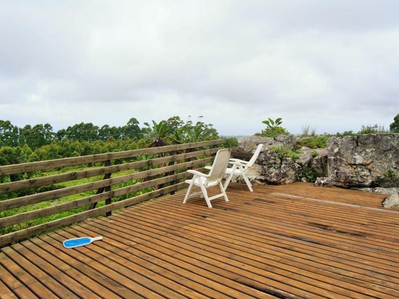 An elevated timber deck featuring a natural rock formation and wooden balustrade, offering expansive views of the surrounding farm landscape.