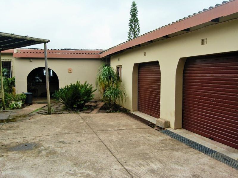 Exterior view of a farm property featuring a double garage with roll-up doors, a concrete driveway, and a covered entrance area.