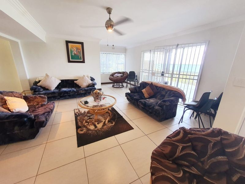 Spacious living room featuring neutral tiled flooring, a ceiling fan, and large sliding glass doors with security gates leading to an outdoor area.