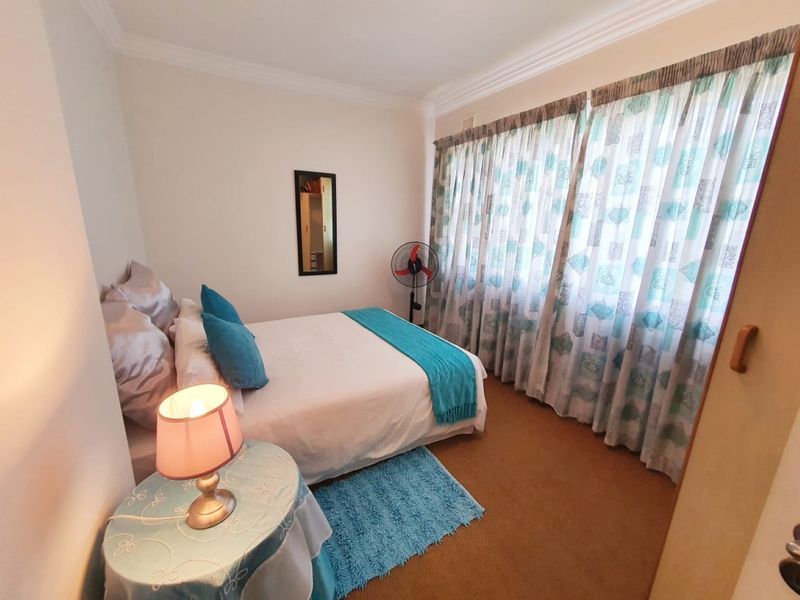 A standard bedroom featuring neutral walls, carpeted flooring, and large window curtains.