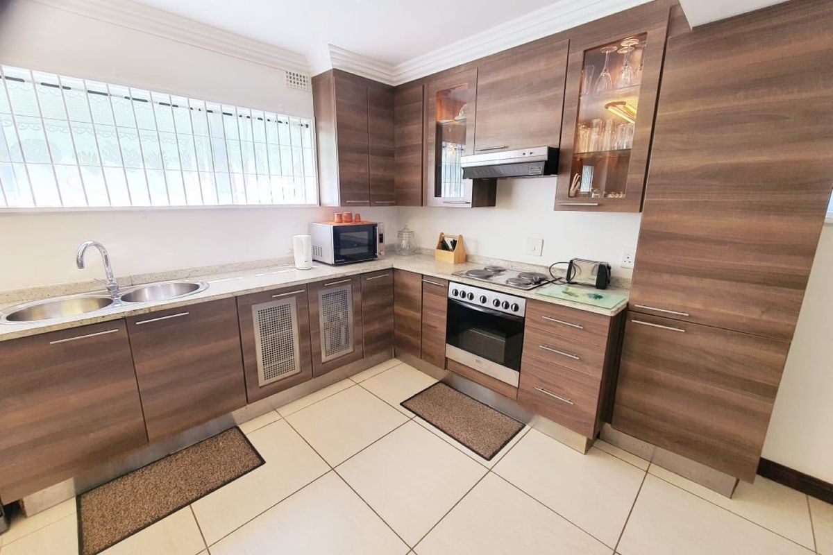 A well-maintained kitchen featuring modern wood-grain cabinetry, stone countertops, integrated appliances, and large floor tiles.