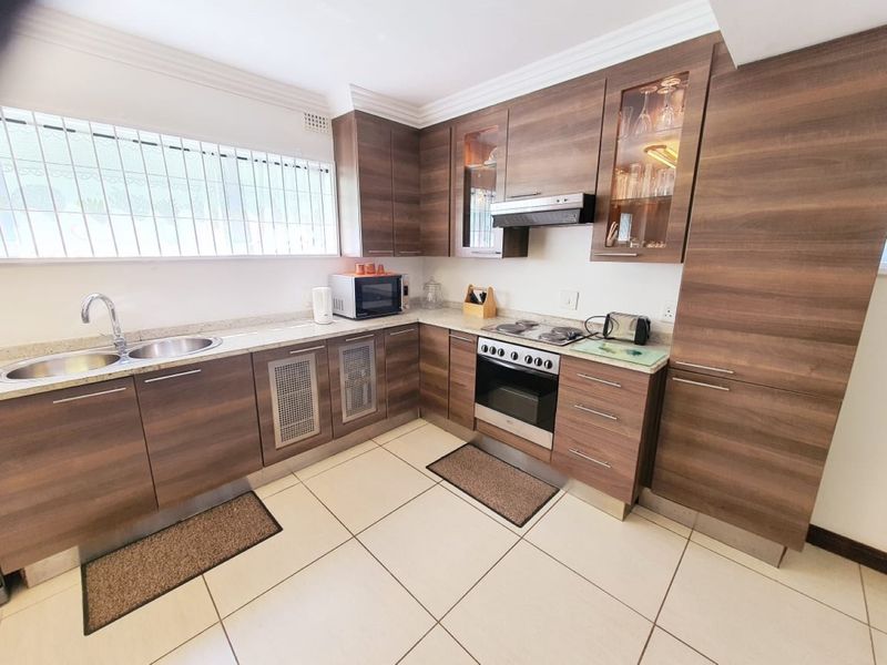 A well-maintained kitchen featuring modern wood-grain cabinetry, stone countertops, integrated appliances, and large floor tiles.