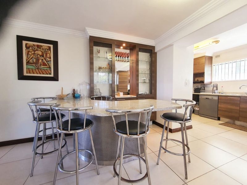 Open plan kitchen and dining area featuring a built-in bar with granite countertop, display cabinetry, and modern ceramic floor tiles.