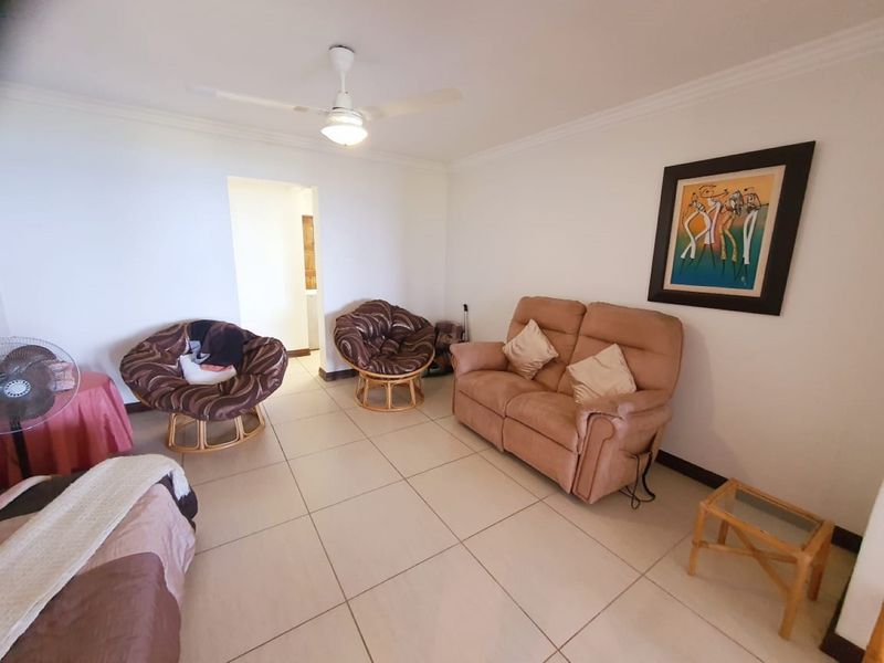 A spacious living room featuring neutral tiled flooring, a ceiling fan, and classic cove cornicing, offering a clean and functional living space.