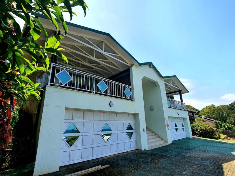 Front elevation of a multi-level house featuring a double garage, upper-level balconies with decorative railings, and a paved driveway.