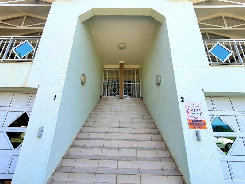 Front entrance featuring a central tiled staircase leading to a secure doorway, flanked by garage doors and upper-level balconies.