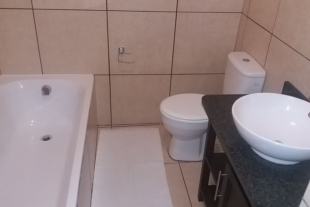 A functional bathroom featuring a white bathtub, a standard toilet, and a modern vessel sink mounted on a dark vanity cabinet with tiled walls.