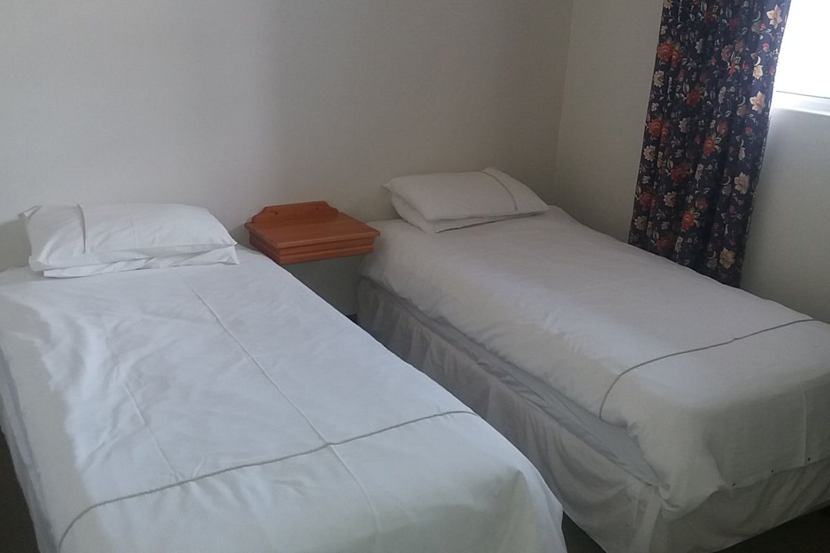 A bedroom featuring a wall-mounted bedside shelf and a window with curtains.