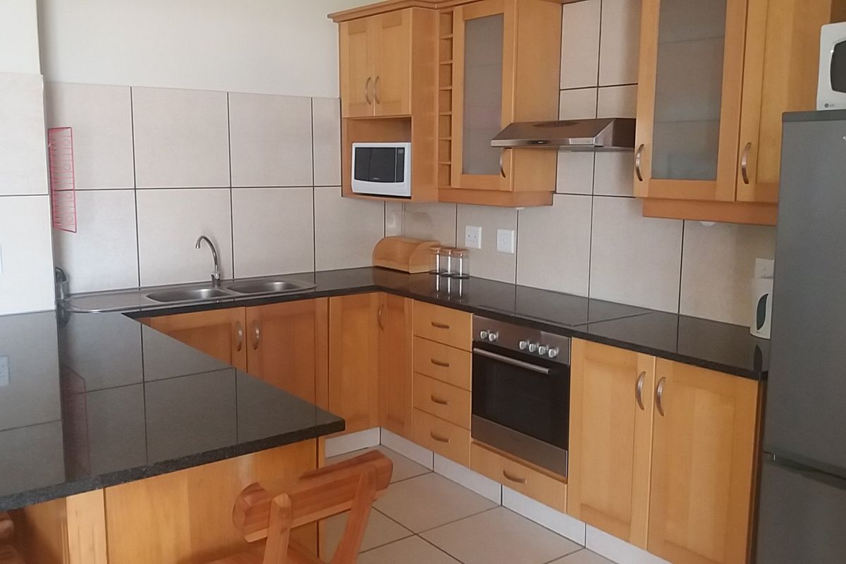A functional kitchen featuring light wood cabinetry, dark granite countertops, a built-in oven, extractor fan, and a double sink with tiled splashbacks.