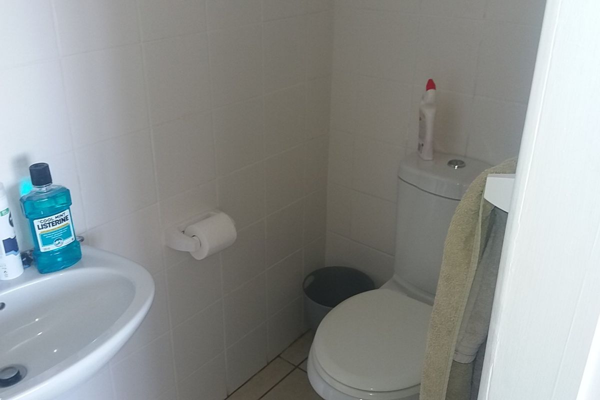 A compact bathroom featuring white wall tiles, a pedestal basin, and a standard toilet.