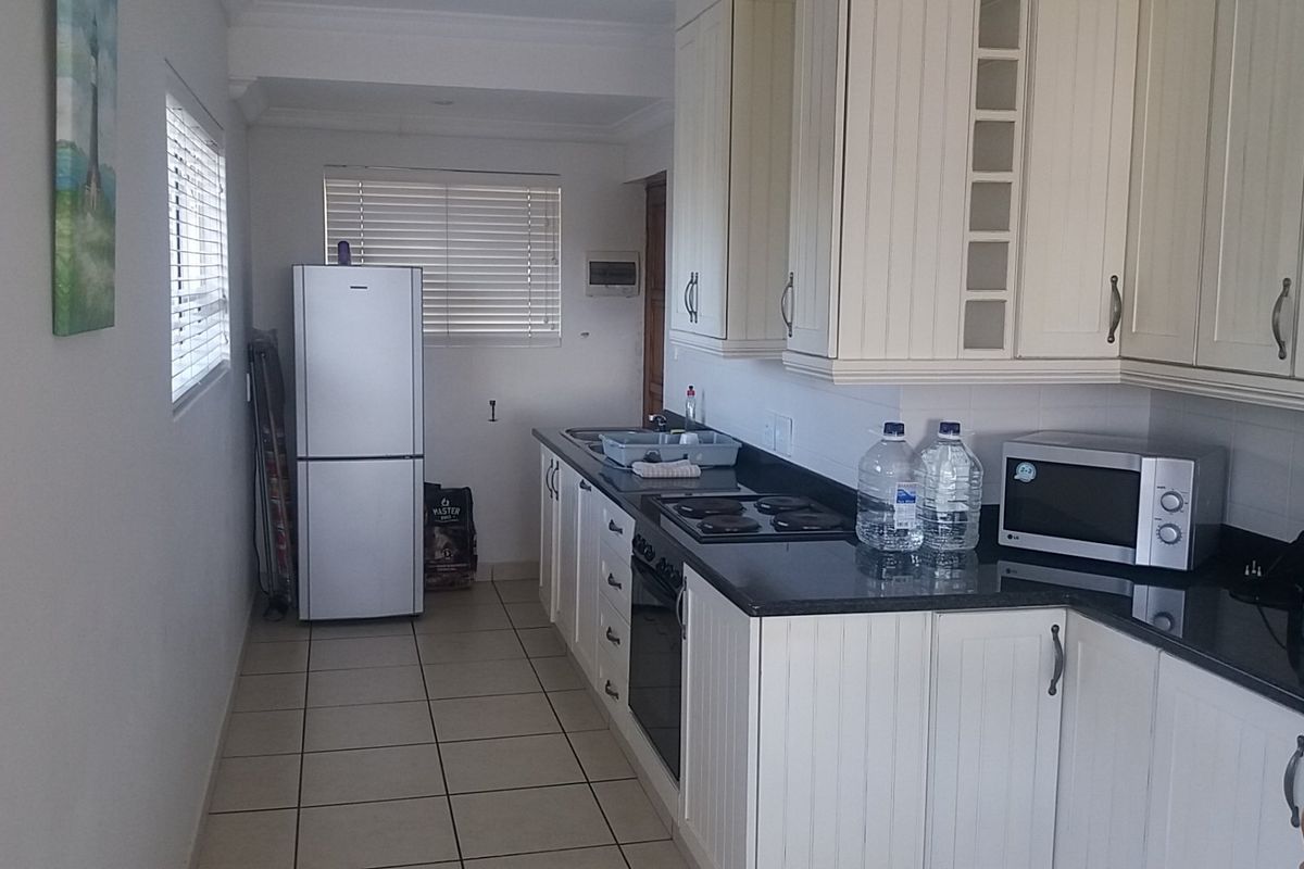 A functional kitchen featuring white cabinetry, dark granite countertops, an integrated hob and oven, and tiled flooring with natural light from window blinds.