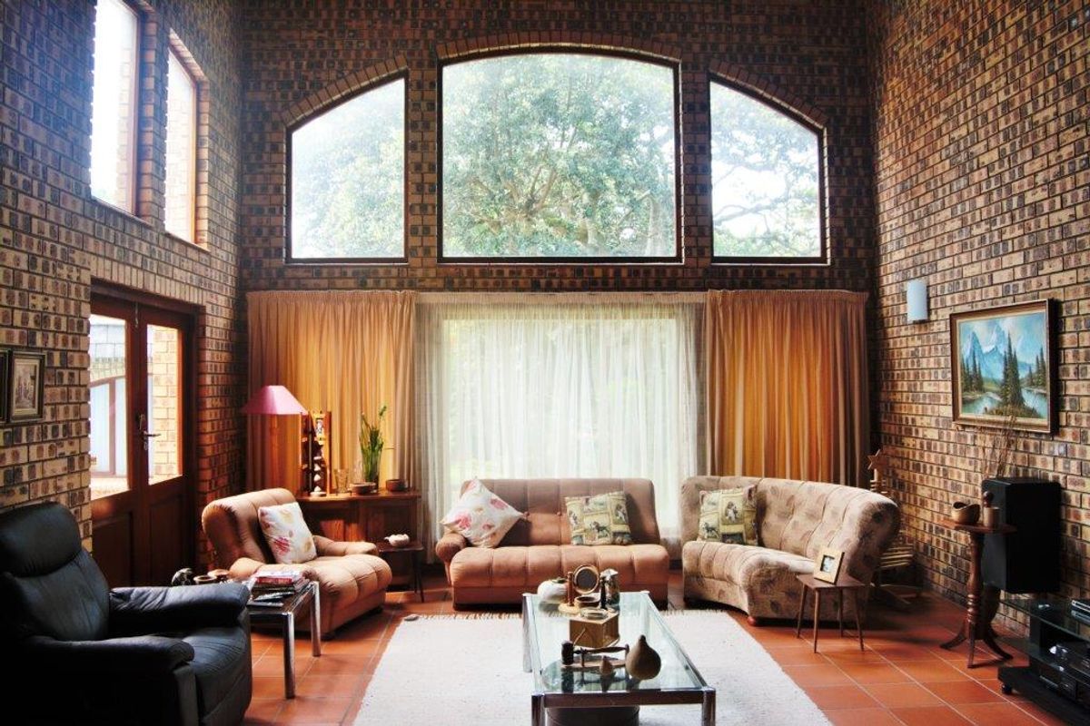 Spacious living room featuring double-height exposed brick walls, terracotta flooring, and large arched windows that provide abundant natural light.