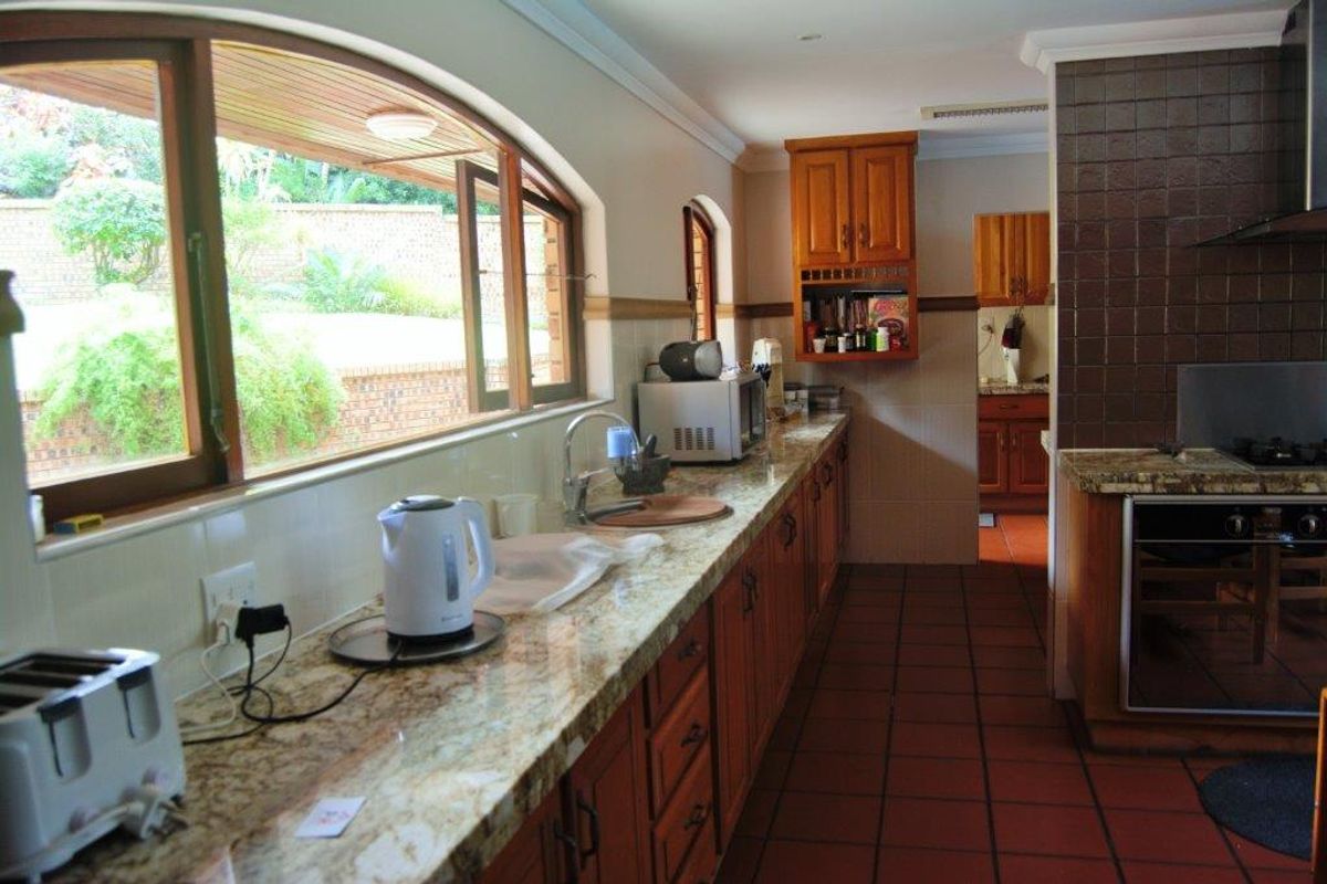 A functional kitchen featuring granite countertops, wooden cabinetry, built-in oven, and gas hob, with large arch-top windows providing natural light and garden views.