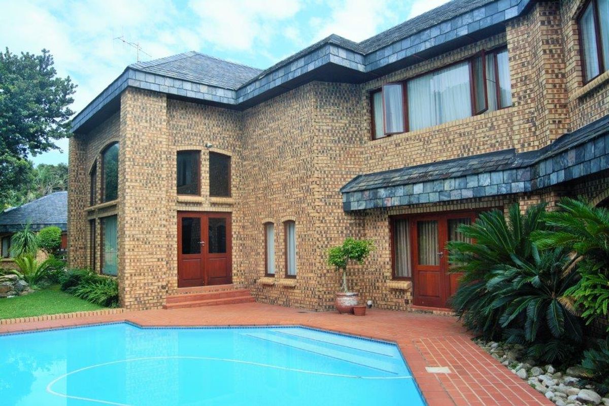 Rear view of a double-story brick house featuring a swimming pool, terracotta patio, and established garden surroundings.