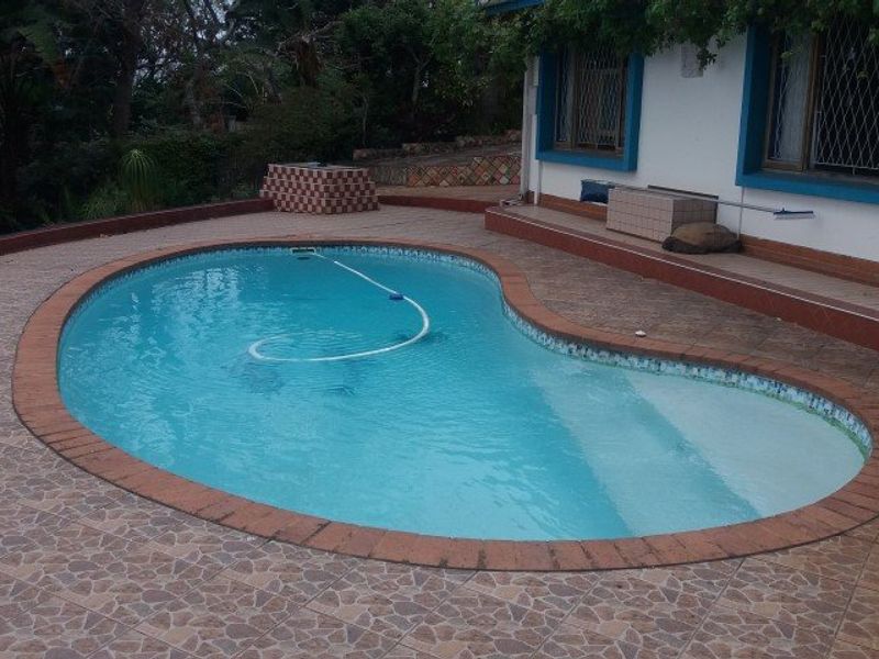 Outdoor pool area featuring a kidney-shaped swimming pool with tiled surround and brick coping, set against the rear facade of the house.