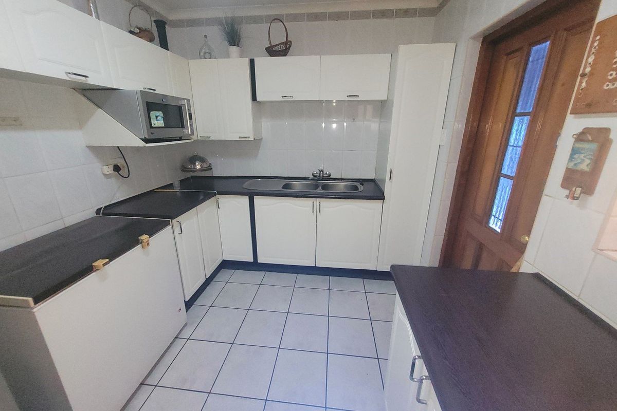 A functional kitchen featuring white cabinetry, dark laminate countertops, tiled flooring, and a built-in microwave, providing a practical workspace with classic finishes.