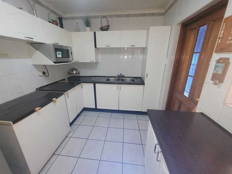 A functional kitchen featuring white cabinetry, dark laminate countertops, tiled flooring, and a built-in microwave, providing a practical workspace with classic finishes.