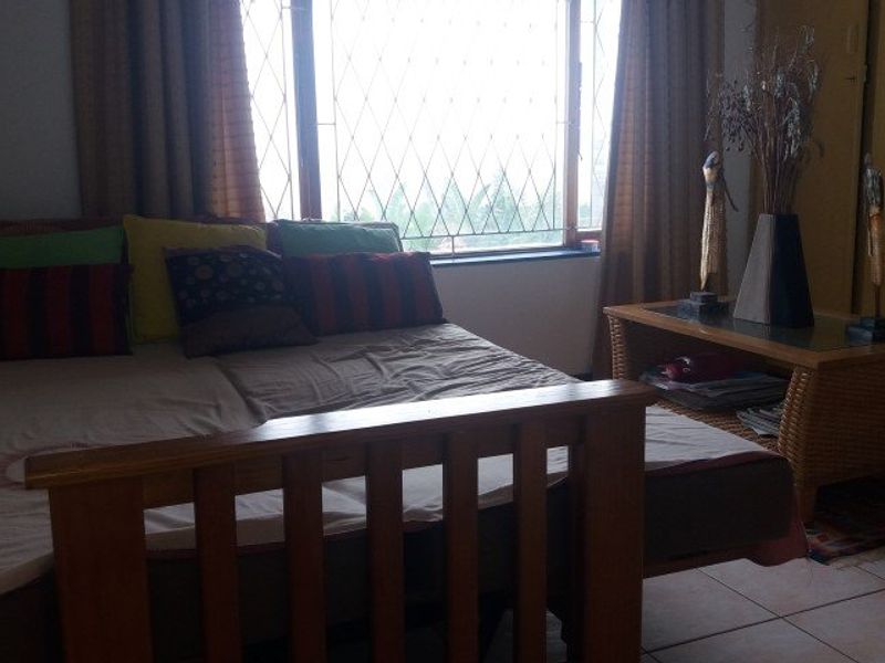 A bedroom featuring tiled flooring, a built-in wardrobe, and a large window fitted with security bars.