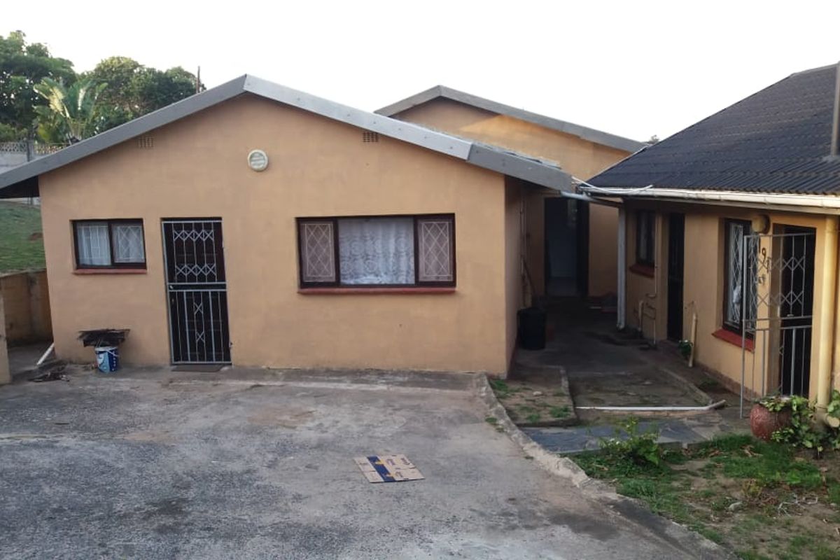 Rear exterior view of the property featuring a concrete driveway, security gates, and a tiled roof structure with weathered exterior finishes.