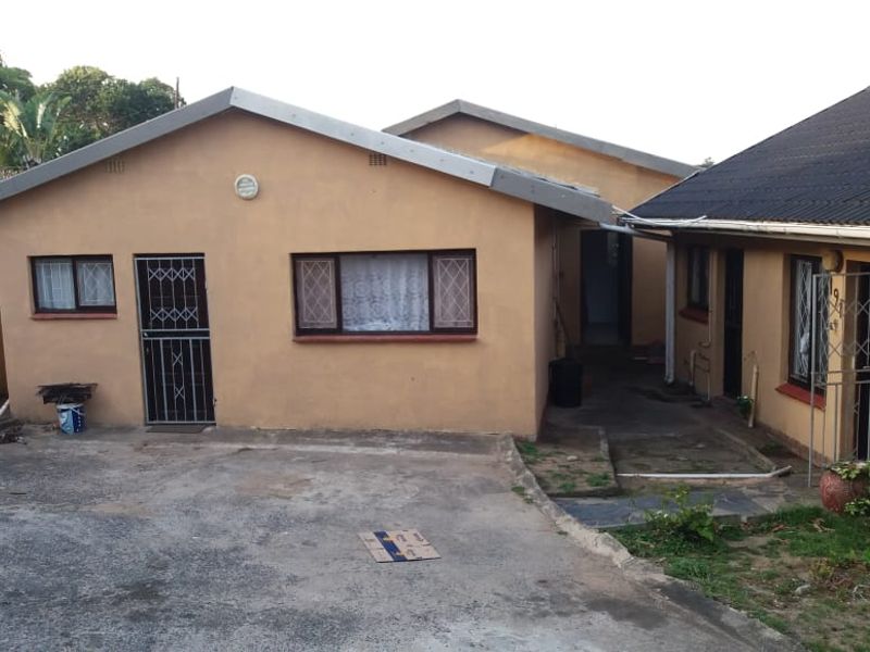 Rear exterior view of the property featuring a concrete driveway, security gates, and a tiled roof structure with weathered exterior finishes.