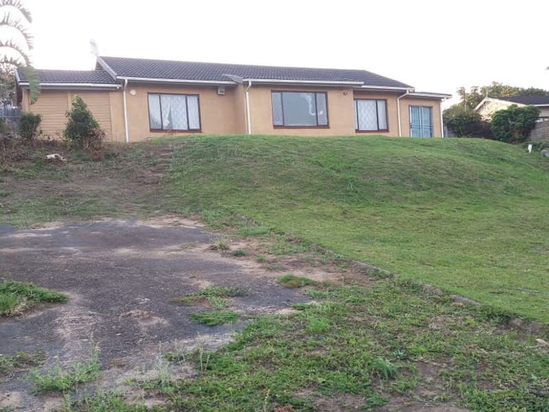 Rear view of a single-story house featuring a tiled roof, large windows, and a spacious backyard with a concrete driveway area.