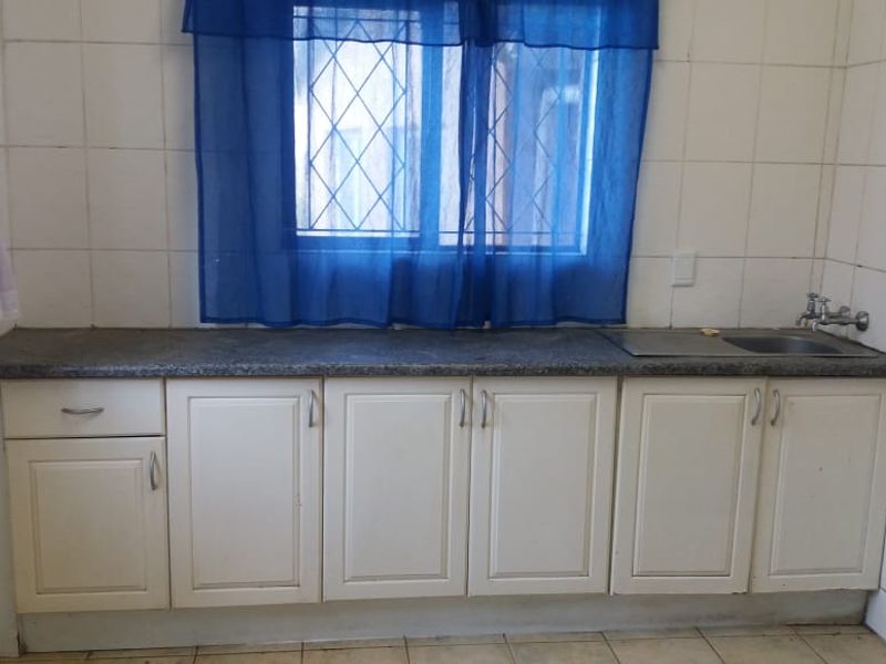A functional kitchen area featuring built-in cabinetry, a stone countertop, and a stainless steel sink, finished with tiled walls and flooring.