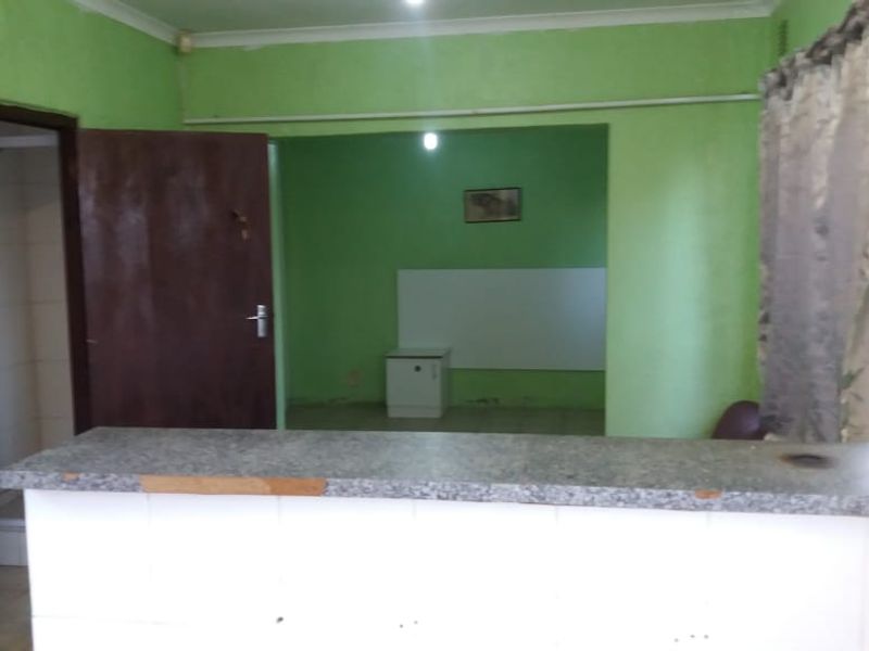 Open plan living area featuring a breakfast bar, tiled counter, and an adjacent shower cubicle, presenting a dated interior in need of cosmetic updates.