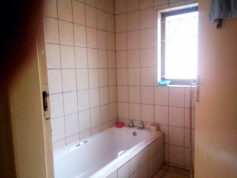 A functional bathroom featuring a built-in bathtub with tiled surround and a window with security bars, requiring cosmetic updates to modernize the space.