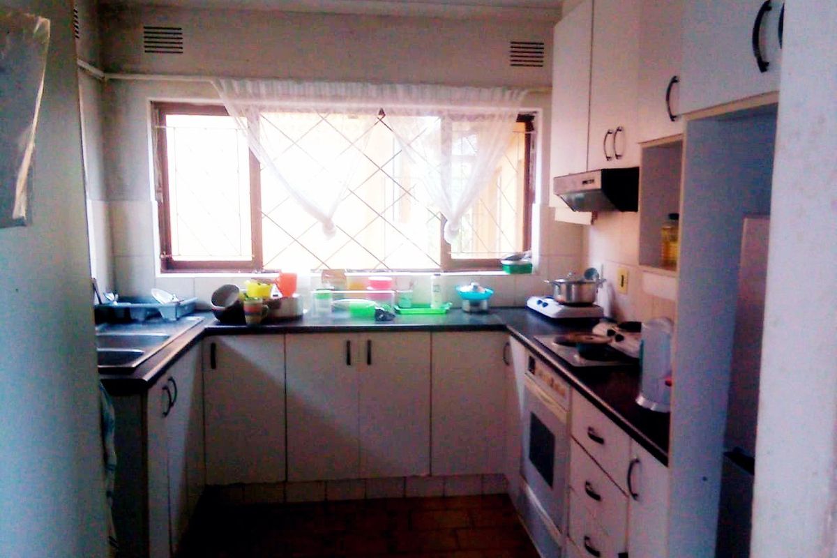 A functional kitchen featuring built-in cabinetry, laminate countertops, a built-in oven, and an extractor fan, with tiled flooring and security bars on the window.