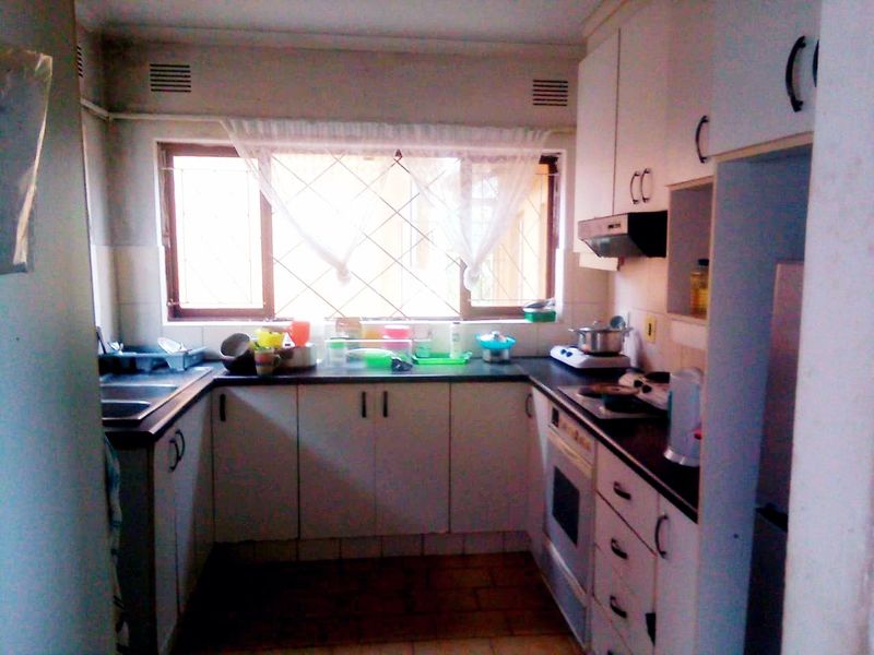A functional kitchen featuring built-in cabinetry, laminate countertops, a built-in oven, and an extractor fan, with tiled flooring and security bars on the window.