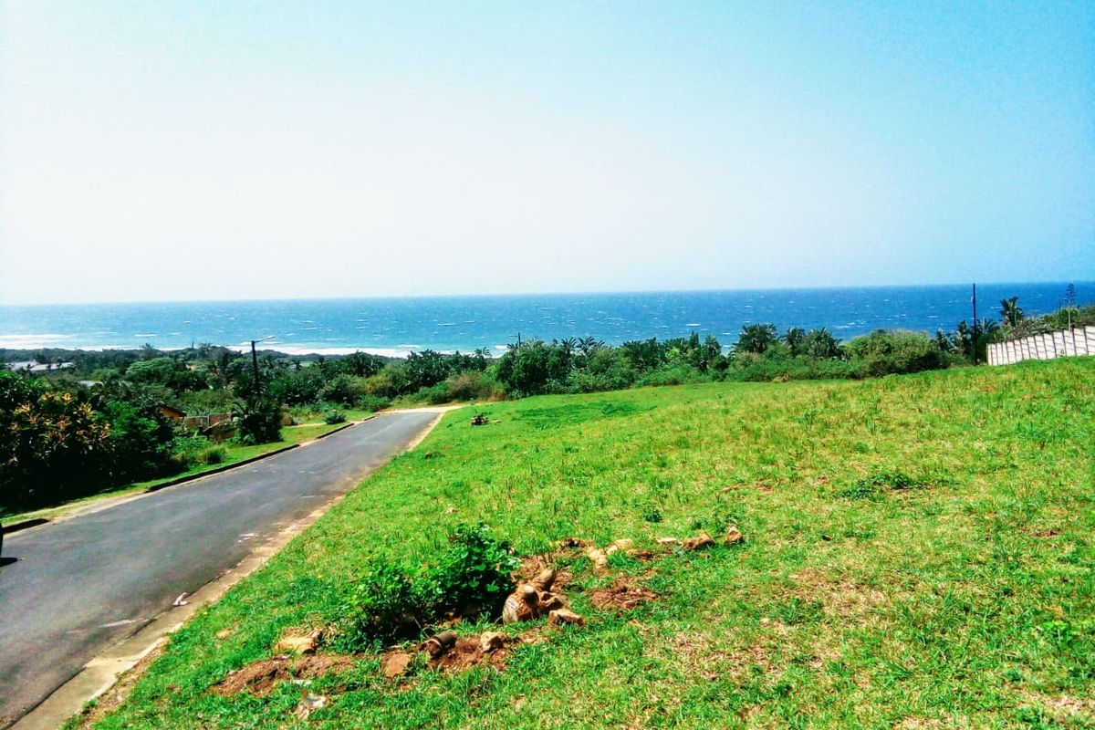 A vacant residential plot featuring a gentle slope, grassy terrain, and an expansive, unobstructed view of the ocean and coastline.
