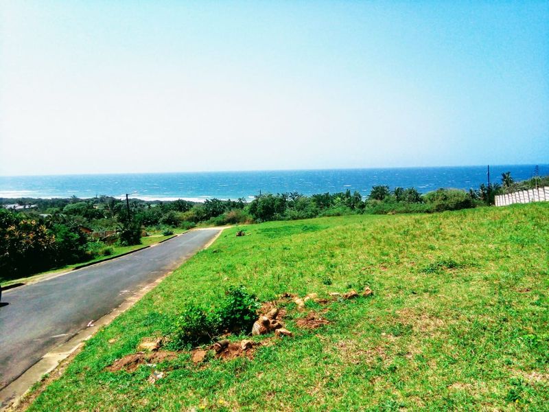 A vacant residential plot featuring a gentle slope, grassy terrain, and an expansive, unobstructed view of the ocean and coastline.
