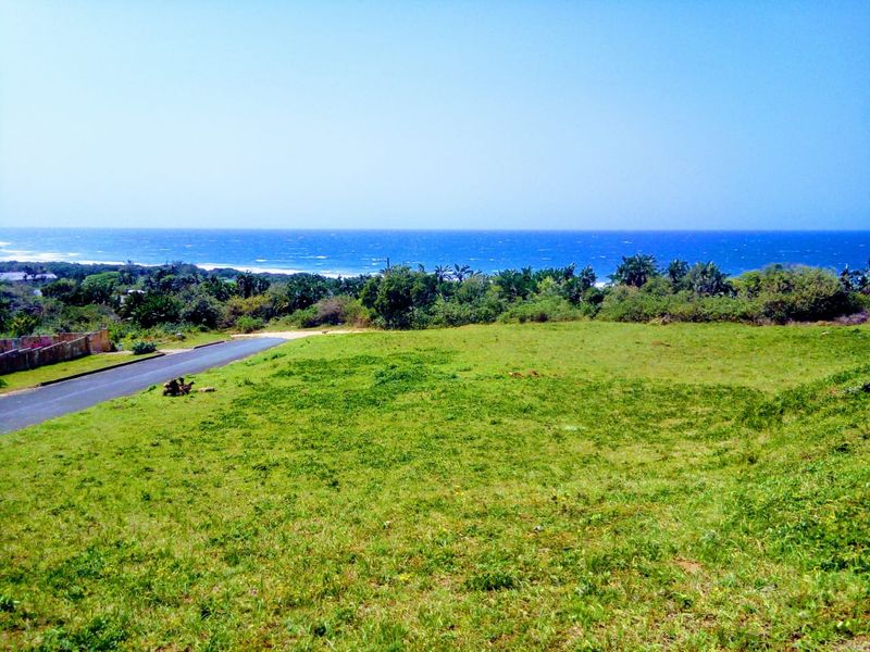 A vacant residential plot featuring expansive green space and a scenic ocean view, situated adjacent to a paved access road.