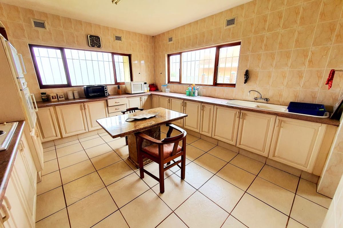 Spacious kitchen featuring tiled walls and flooring, ample built-in cabinetry, a central island, and integrated appliances, offering a functional layout with dated finishes.