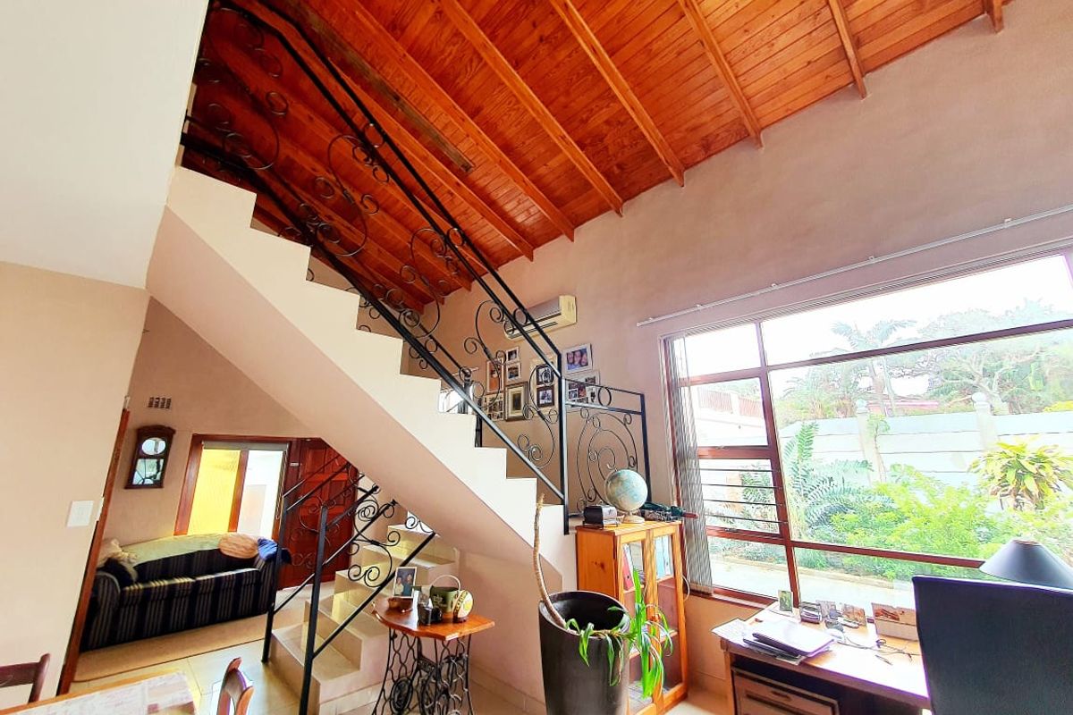 Spacious living area featuring a high exposed timber rafter ceiling, wrought iron staircase, and large windows providing ample natural light.