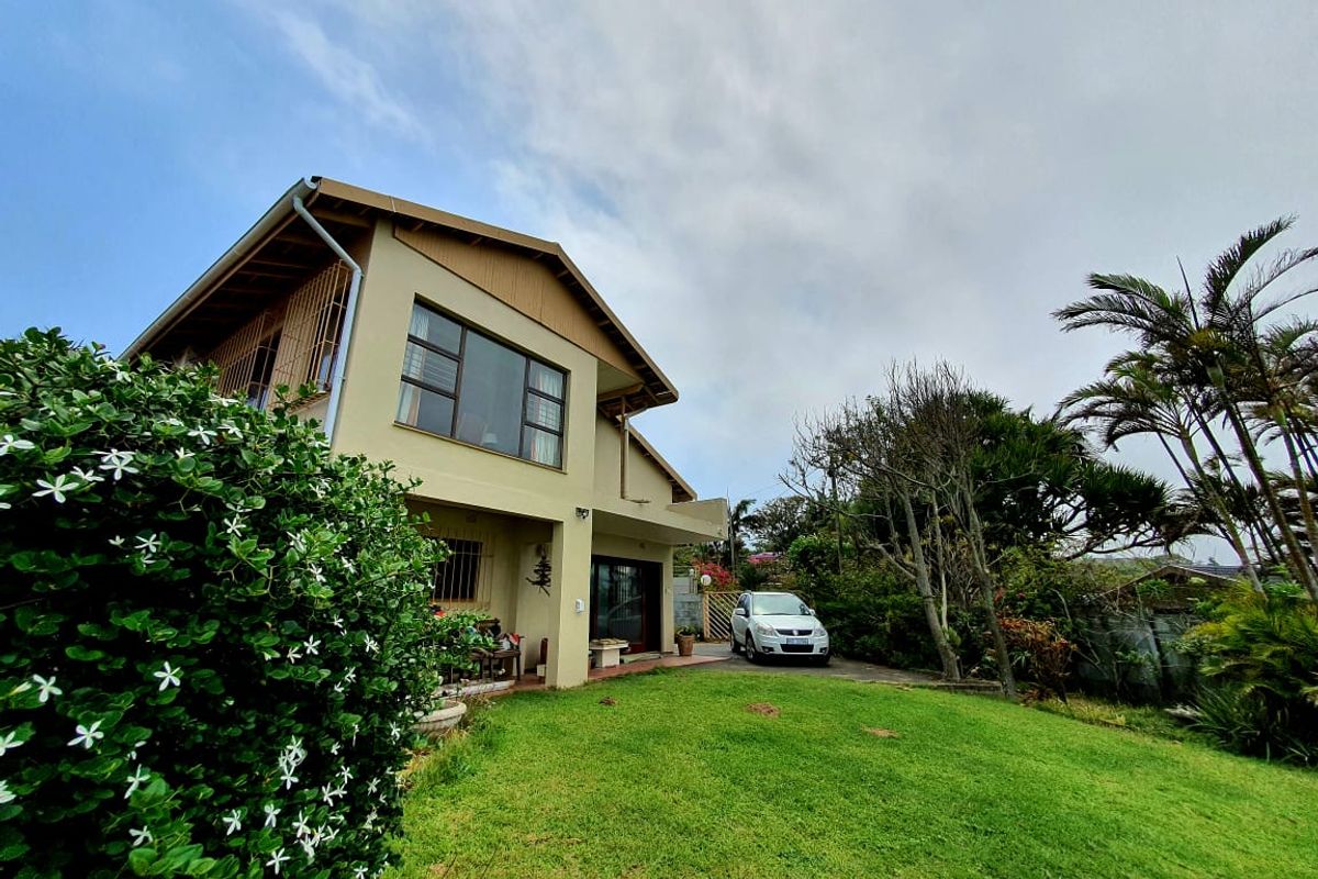 Rear view of a two-story residential house featuring a well-maintained lawn, paved driveway, and large windows.