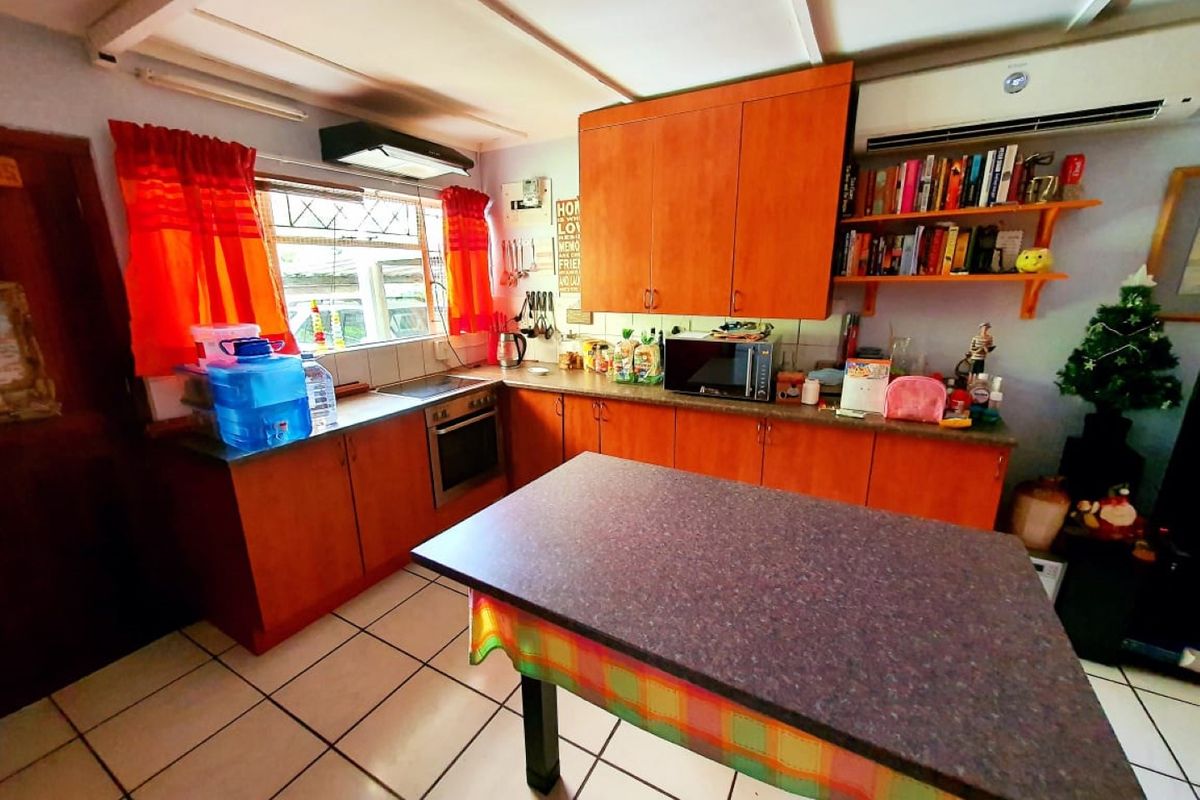 A functional kitchen featuring wooden cabinetry, built-in oven and hob, extractor fan, and tiled flooring, with an integrated air conditioning unit.