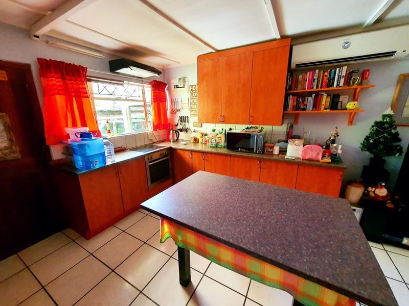 A functional kitchen featuring wooden cabinetry, built-in oven and hob, extractor fan, and tiled flooring, with an integrated air conditioning unit.