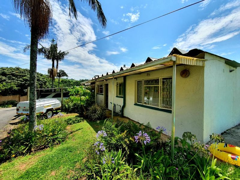 Front exterior view of a townhouse featuring a covered patio area, security window bars, and established garden surroundings.