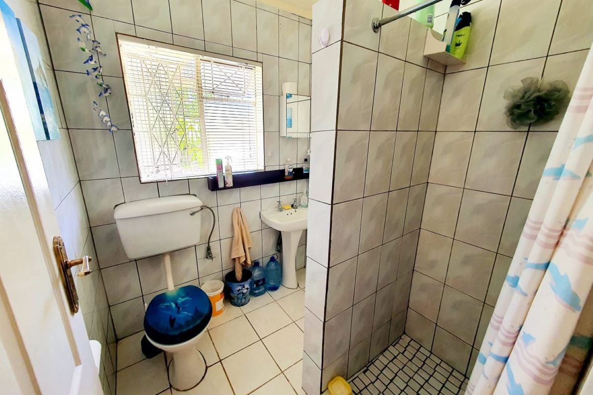 A functional bathroom featuring a tiled shower enclosure, pedestal basin, and toilet, with neutral wall and floor tiling throughout.