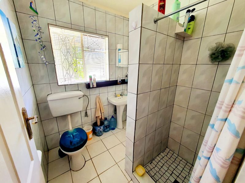 A functional bathroom featuring a tiled shower enclosure, pedestal basin, and toilet, with neutral wall and floor tiling throughout.