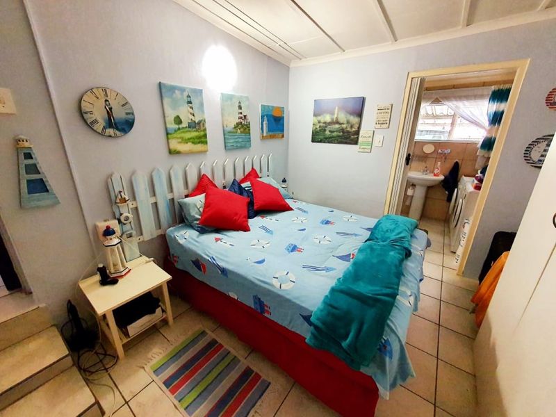 A bedroom featuring tiled flooring and an exposed beam ceiling, with direct access to an adjoining bathroom area.