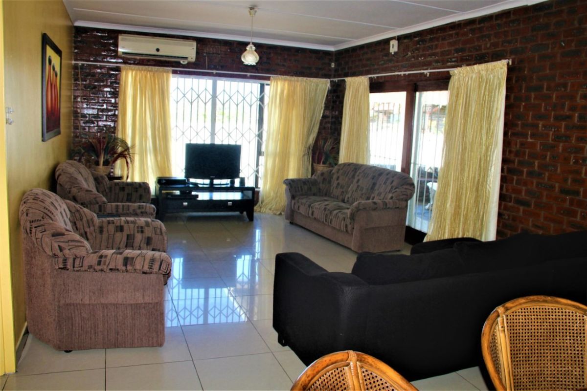 Spacious living room featuring polished floor tiles, exposed brick feature walls, and a wall-mounted air conditioning unit.