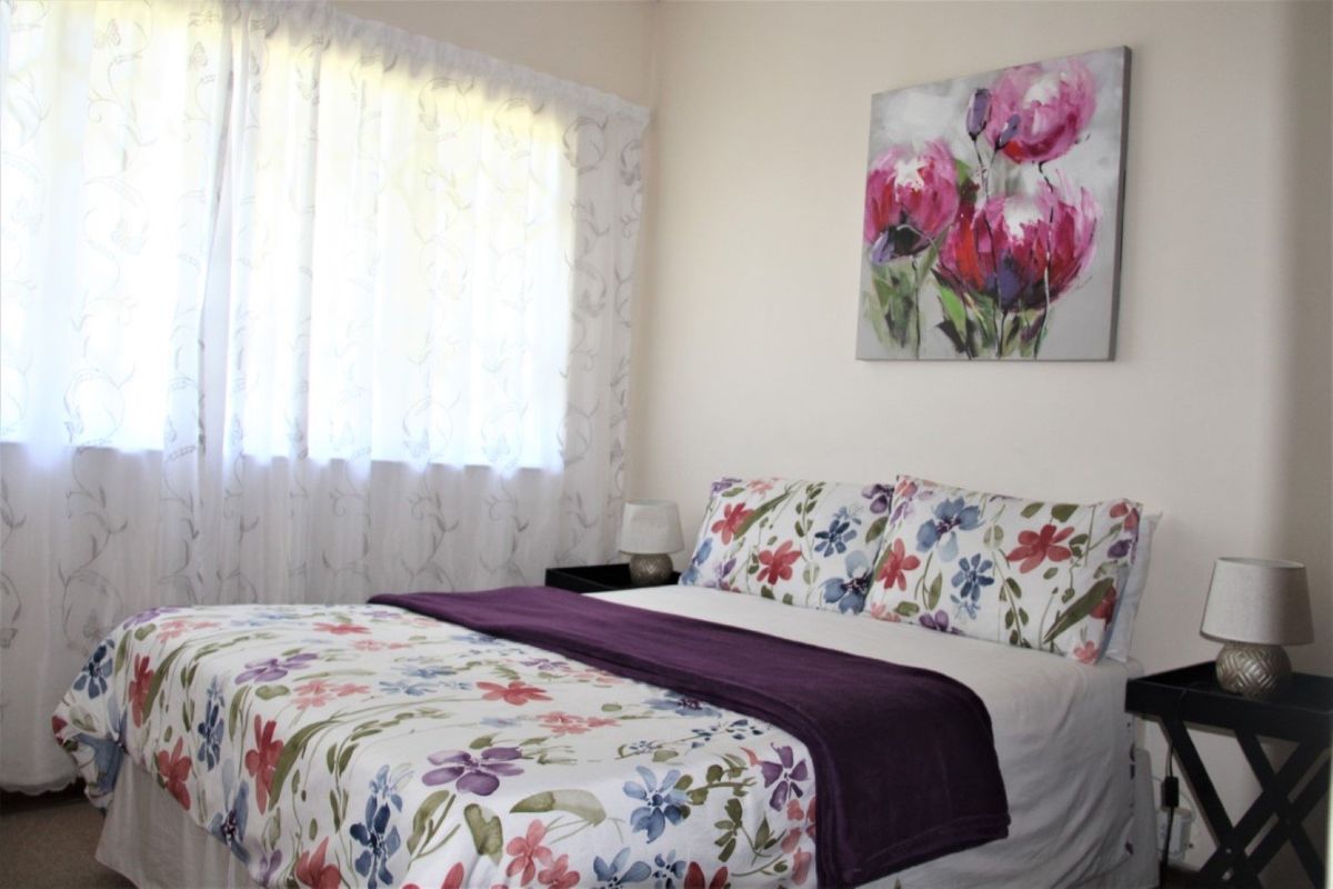 A cozy bedroom featuring neutral walls, carpeted flooring, and a window with sheer curtains, providing a comfortable and functional living space.