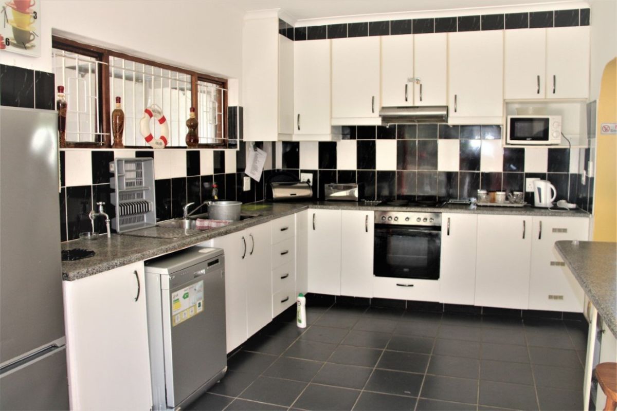 A functional kitchen featuring white cabinetry, granite countertops, a built-in oven with extractor fan, and a contrasting black and white tiled backsplash.