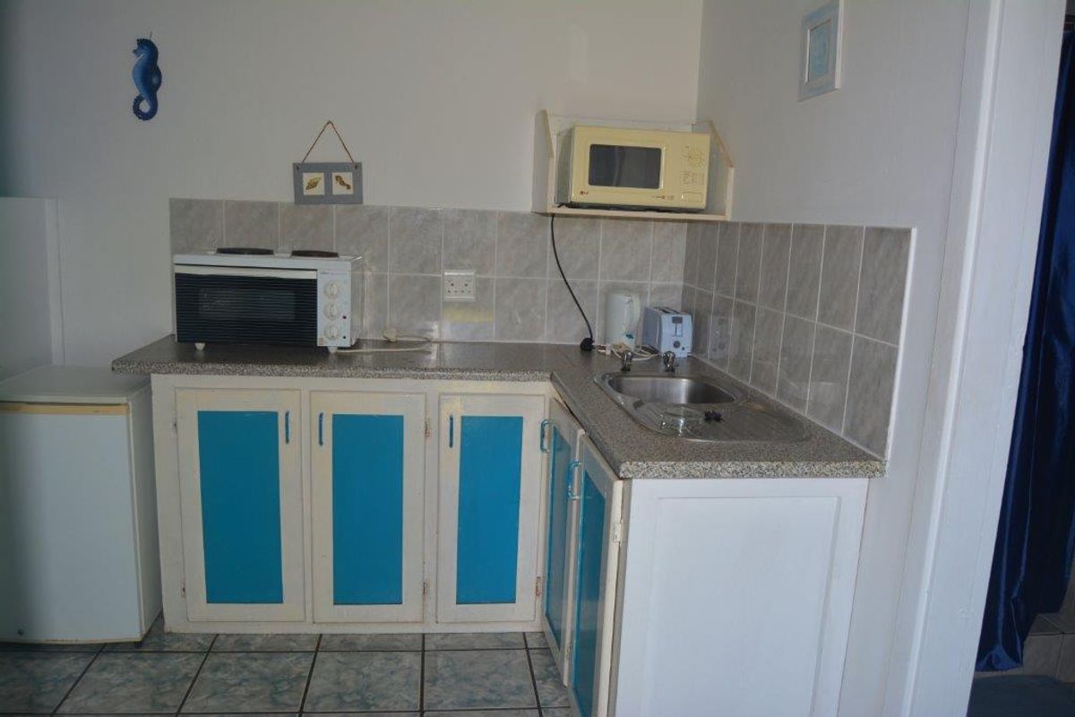 A compact kitchenette featuring laminate countertops, a stainless steel sink, and built-in cabinetry with a tiled backsplash.
